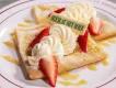 Butterbier™ Crepes  Zwei geviertelte Crêpes mit Schlagsahne, gelber Soße und Erdbeerscheiben.