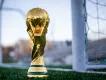 FIFA 2026 World Cup A gold trophy with a globe at the top and things wrapping around it sat in front of a white football goal.