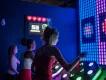 Activate Orlando Girl pressing a gaming pad in front of a screen with a game on it. There are two other players and on the wall it displays their lives left.