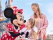 A young girl and her mother smiling with the Minnie Mouse character in front of Sleeping Beauty Castle at Disneyland Paris.