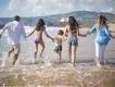 Family enjoying a summer beach holiday in Europe, running into the ocean together