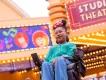 Guest in a wheelchair wearing Minnie Mouse ears smiling beneath the Studio Theater marquee at Production Courtyard, Disney Adventure World