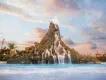 A wide shot of a massive artificial volcano with cascading waterfalls flowing into a large, wavy blue pool, under a pastel pink and blue sunset sky with scattered clouds
