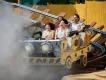 Riders smiling and cheering aboard a rustic mine cart roller coaster emerging from a cloud of mist
