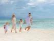 A family dressed in white holding hands and running along a tropical white-sand beach