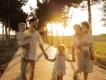 A happy family of five holding hands and carrying young children while walking along a paved path at sunset