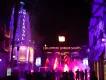 A crowd of guests walking toward the brightly lit Halloween Horror Nights entrance gate with bursts of fire in the night sky