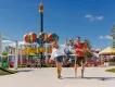 A mother and father swinging their young son by his arms while walking in front of a Peppa Pig balloon ride at a theme park
