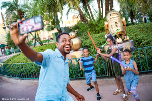 A father and three children taking a selfie posing with lightsabers in front of the Star Wars golden statues
