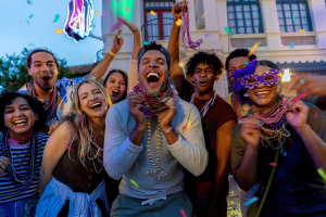 A group of friends in their twenties smiling and laughing at the camera, wearing lots of Mardi Gras beads