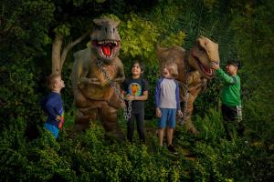4 children standing in some foliage with two dinosaur animatronics