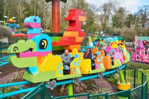 Adults and young children riding a rollercoaster designed to look like a dinosaur made with colourful DUPLO bricks
