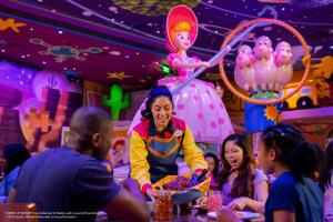 A server bringing a basket full of food to a table of 2 adults and 2 children. There is Toy Story theming in the background including a figure of Bo Peep