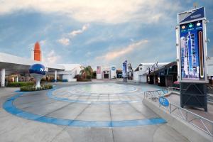 A paved plaza surrounded by space themed buildings, with a large model of the NASA logo to the left-hand side