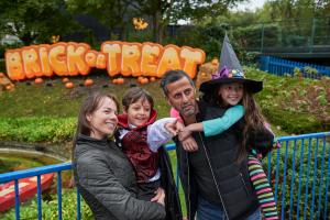 A family posing in front of a sign reading "Brick or Treat". The two children are dressed in Halloween costumes