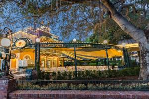 The exterior of a restaurant with white chairs and tables covered by a green and yellow striped awning and green ironwork