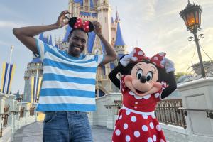 A man wearing Minnie ears standing with Minnie Mouse in front of Cinderella Castle