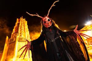A blood-covered figure with long fingers and horns and large eye sockets looking down at the camera