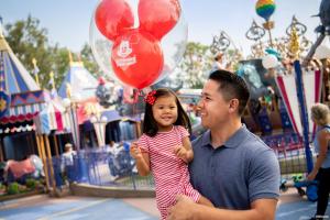 A man holding a young girl who is carrying a balloon standing in front of Dumbo the Flying Elephant