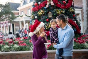 A man holding a small boy who is smiling at a woman eating a cookie and wearing a Santa hat