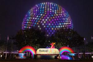 Spaceship Earth lit up in rainbow colours behind a sign reading Festival of the Arts