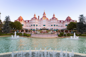 The exterior of a pink hotel behind a fountain and a flower bed in the shape of Mickey Mouse