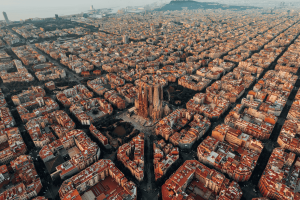 Layout of Barcelona with a view of the Sagrada Familia cathedral. The city is laid out with straight roads and buildings shaped in squares. They all have the same colour scheme with white and orange walls and roofs.