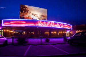 A neon sign reading Hotel Santa Fe underneath a large picture of Lightning McQueen and Sally from Cars