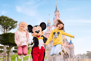 Two young girls jumping with Mickey Mouse in front of the Disneyland Paris castle