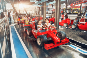 Small kids sat on rollercoaster car which is shaped like a red Ferrari Formula 1 car