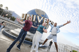 Three people jumping excitedly in front of the Universal Globe