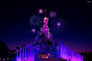 Castle lit neon pink in the night sky with purple fountains below. There are also pink fireworks in the sky.