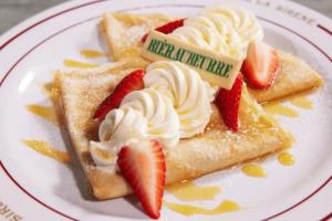 Zwei geviertelte Crêpes mit Schlagsahne, gelber Soße und Erdbeerscheiben.