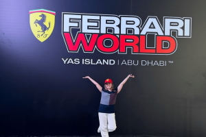 Girl stood in front of Ferrari World sign which has black background, red and white text and the Ferrari logo next to the name.