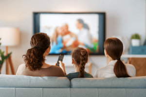 A woman, a teenager and a young girl watching TV from a sofa