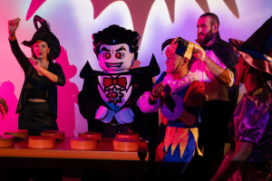 Dracula lego character danging by lego dj deck with kids gethered around wearing halloween costumes.