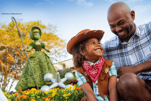 A young boy dressed as a cowboy smiling up at his dad, sat in front of a Bo Peep topiary