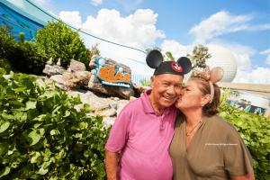 Couple wearing Mickey and Minnie ears near The Seas with Nemo & Friends pavilion at EPCOT, with Spaceship Earth in the background