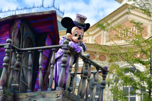 Mickey Mouse in a purple Halloween costume and top hat waving from a balcony at the Disney Halloween Festival