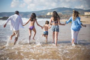 Family enjoying a summer beach holiday in Europe, running into the ocean together