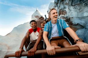 Two young men laughing as they ride the Expedition Everest roller coaster train through snow-covered mountain peaks