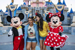 Two friends laughing while posing with Mickey Mouse and Minnie Mouse in front of Sleeping Beauty Castle