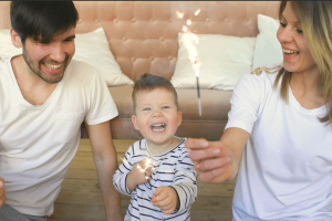 A young family celebrating together at home with sparklers, smiling and laughing