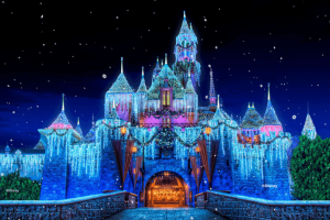 Sleeping Beauty Castle at Disneyland Resort glowing at night with shimmering icicle lights, holiday wreaths, snow-capped turrets, and falling snow effect