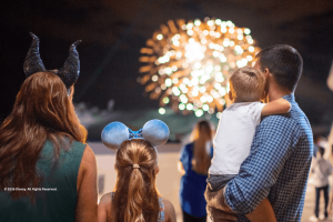 A family wearing Disney ears looking out at a nighttime fireworks display