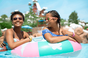 Two smiling women floating together on a colorful inflatable inner tube in a water park pool