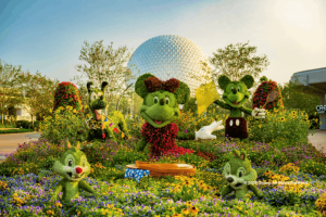 Topiaries of Mickey, Minnie, Pluto, Chip, and Dale set in a colorful garden bed in front of Spaceship Earth