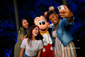 Two guests taking a selfie with Mickey Mouse at night