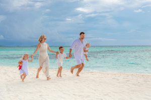 A family dressed in white holding hands and running along a tropical white-sand beach