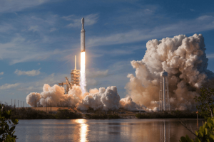 A SpaceX Falcon Heavy rocket launching from the pad, surrounded by large plumes of exhaust
